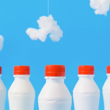 White milk bottles with red caps in front of sky blue background